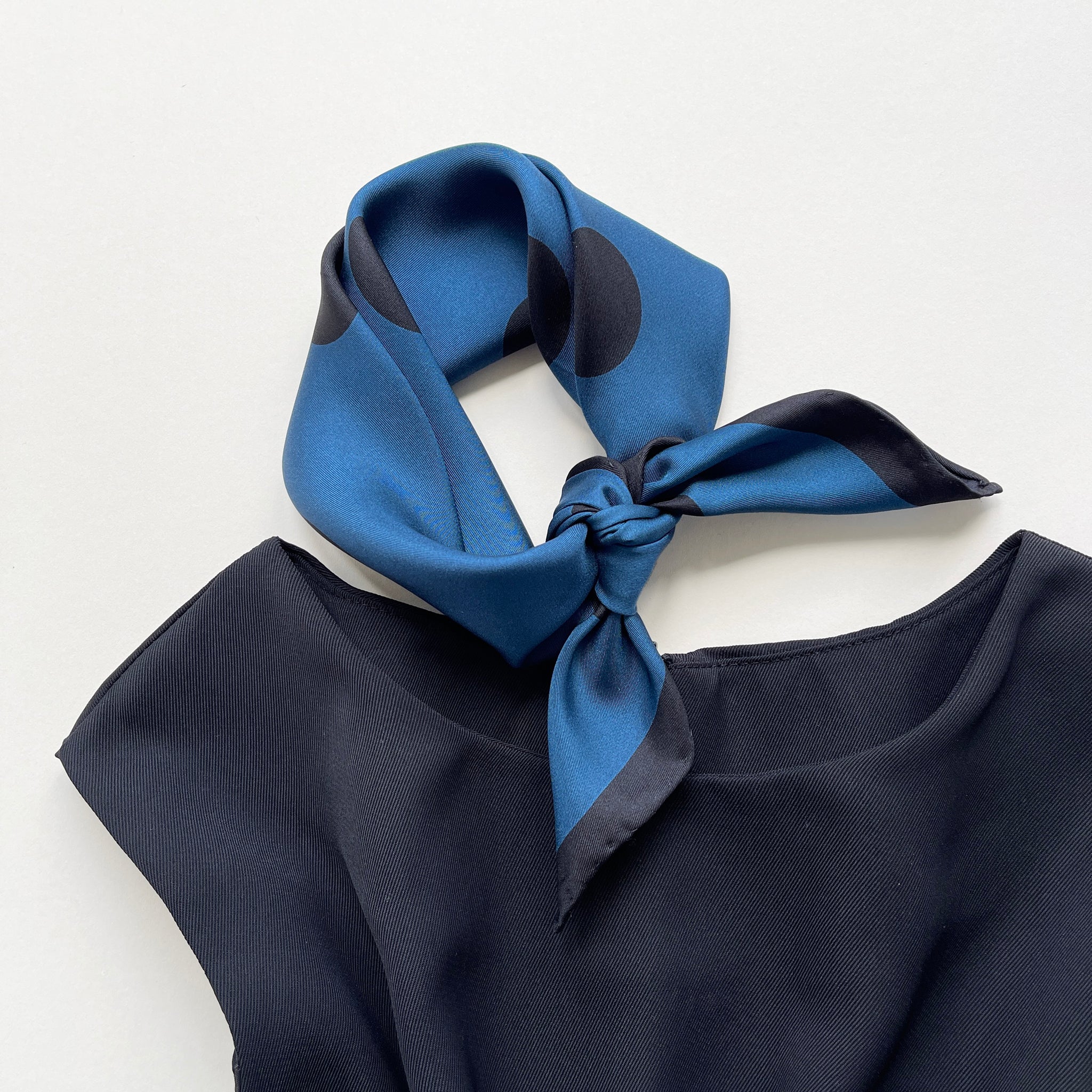 a Yale blue silk bandana scarf featuring black polka dots print, tied as a neckerchief, paired with a sleeveless black dress