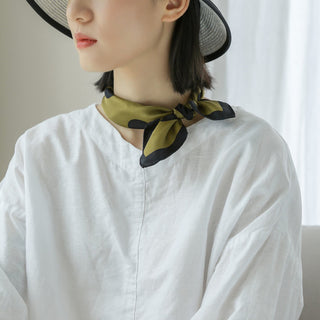 an olive green silk bandana scarf featuring black polka dots print, worn by a women as a neckerchief with white blouse