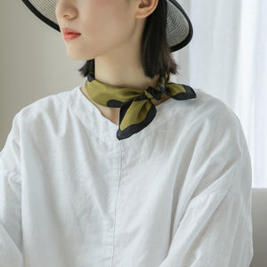 an olive green silk bandana scarf featuring black polka dots print, worn by a women as a neckerchief with white blouse