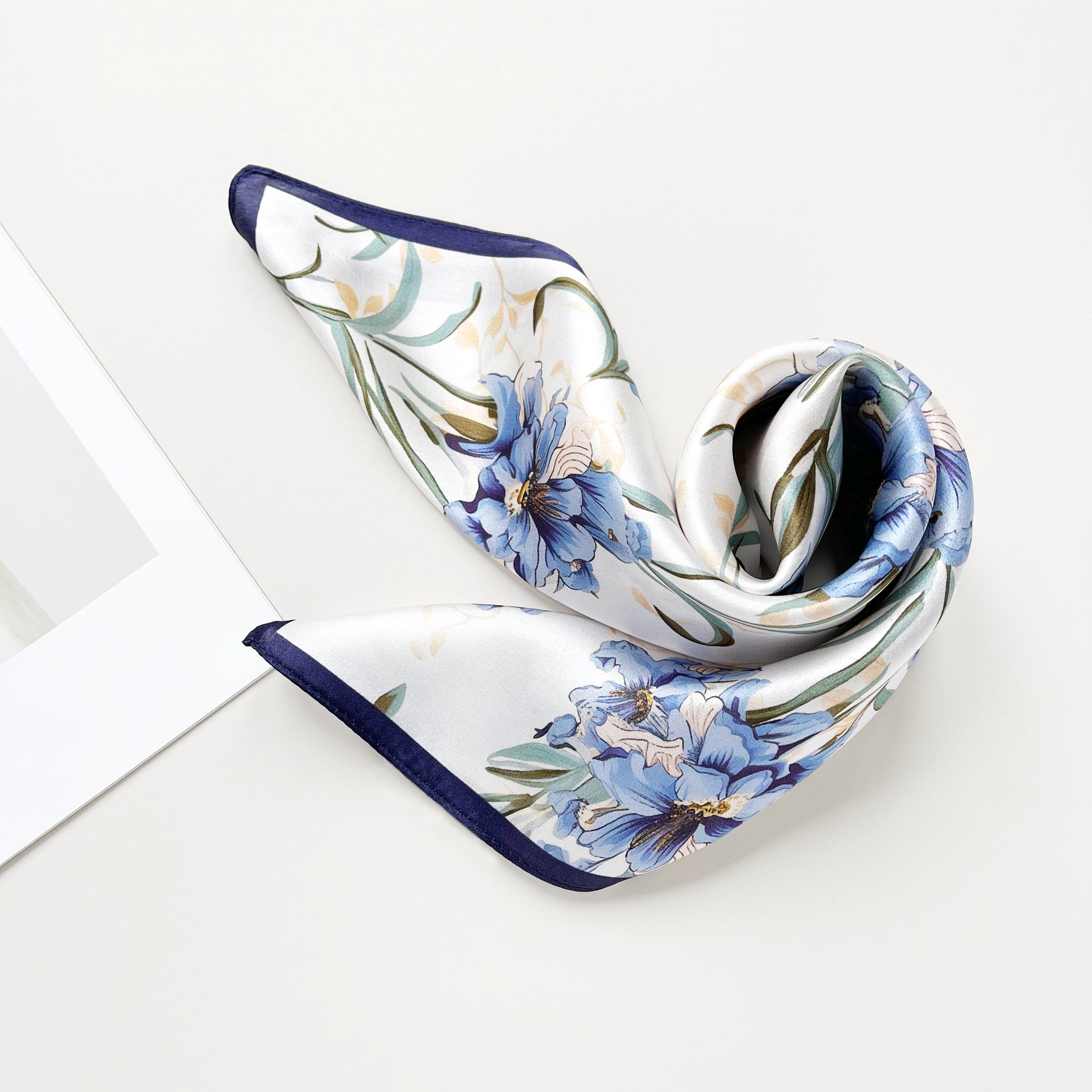 a silk bandana scarf featuring blue bell print with a white base and navy blue edges