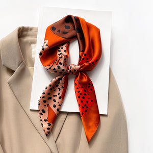 a leopard silk scarf in orange, brown, black and pink hues tied as a classic neckerchief paired with a women's beige suit