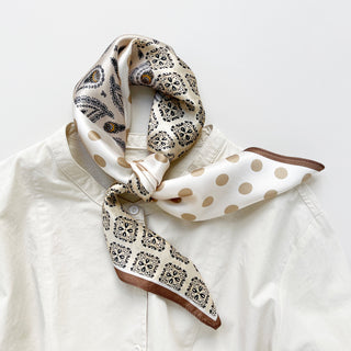 a beige and brown earth tones silk scarf featuring bohemian paisley and polka dot prints with brown edges, knotted as neck scarf, paired with a beige women's turtle neck shirt