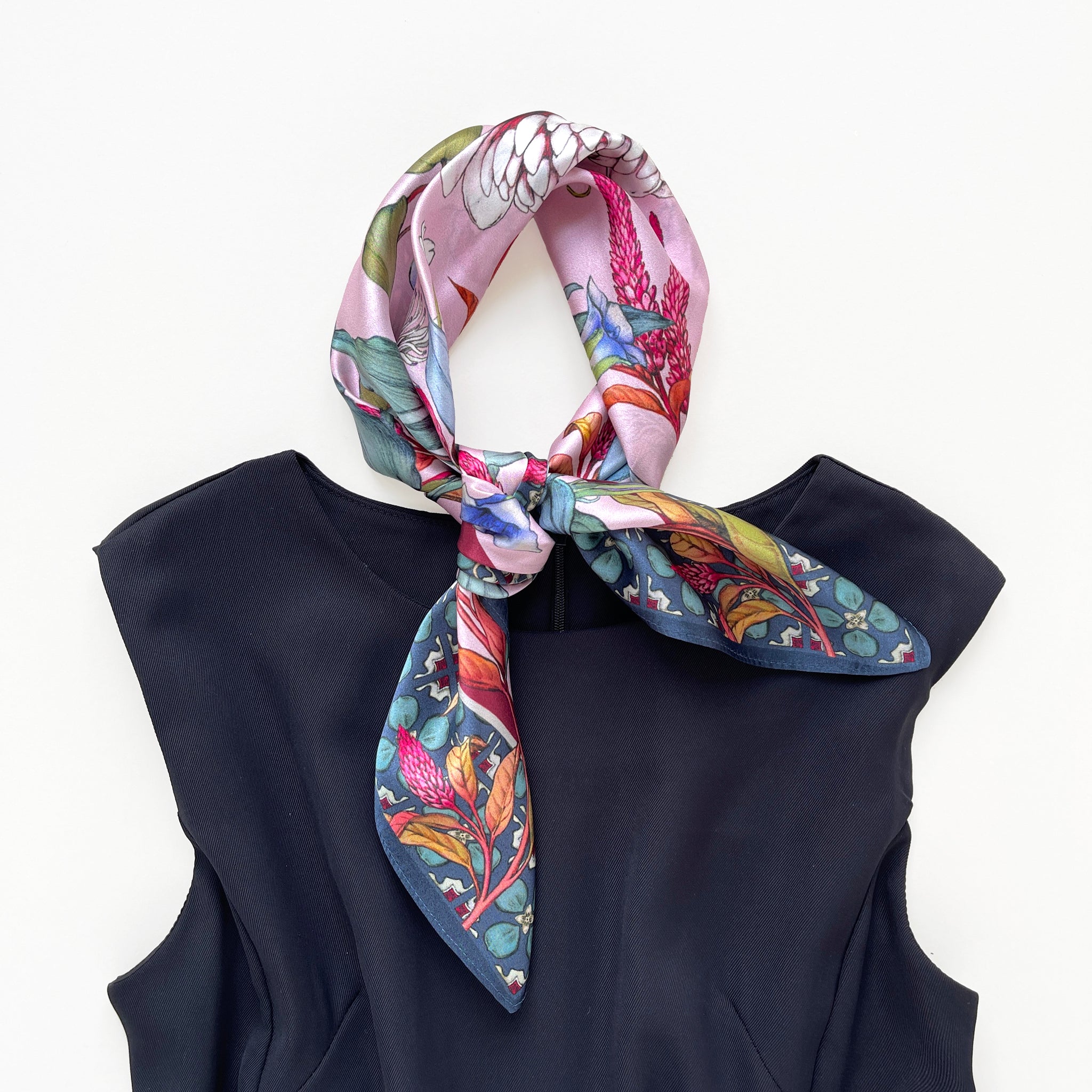 a pink base silk scarf featuring botanic floral print, knotted as a neck scarf, paired with a black dress