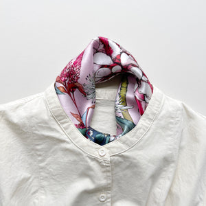 a pink base silk scarf featuring botanic floral print, knotted as a neck scarf, paired with a light beige turtle neck shirt