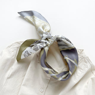 a forest leafy printed square silk scarf in sage green, grey and white tones with hand-rolled edges, knotted as head scarf,  paired with a light beige women's shirt