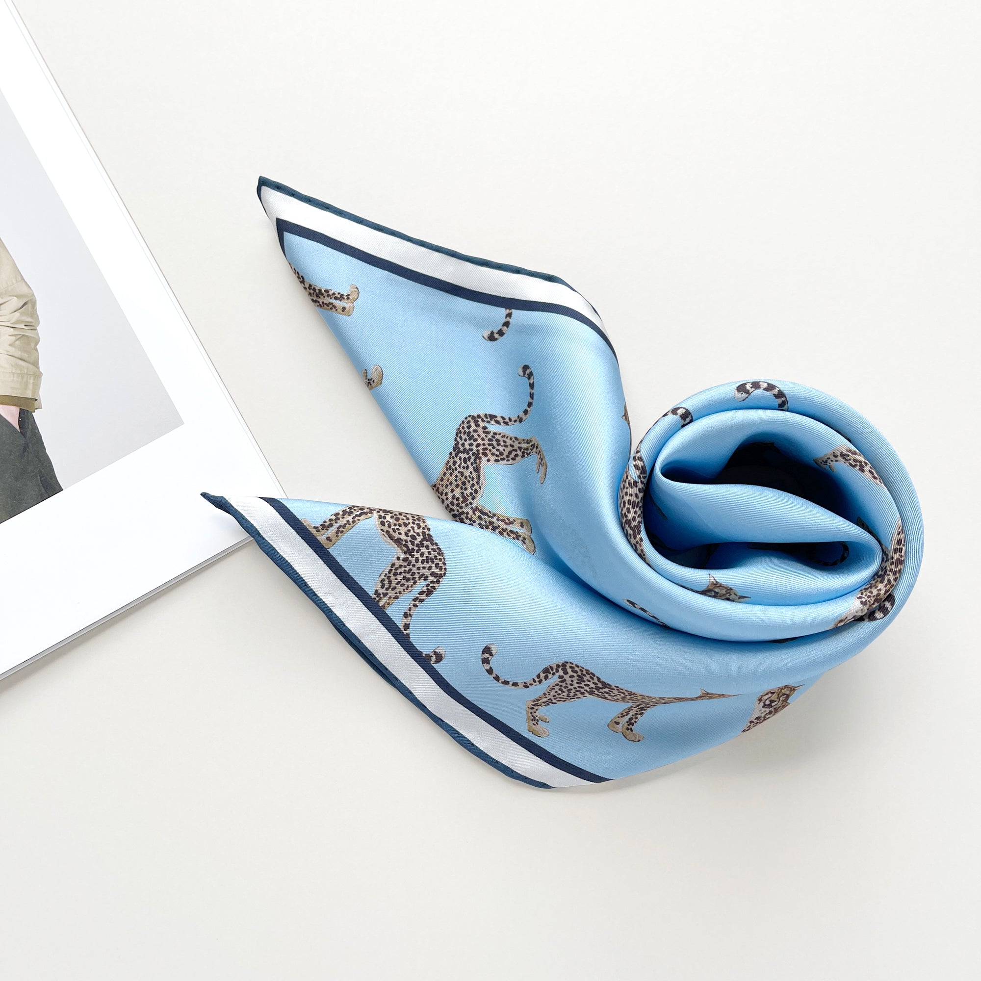 a sky blue base silk scarf featuring leopard print with dark blue hand-rolled edges