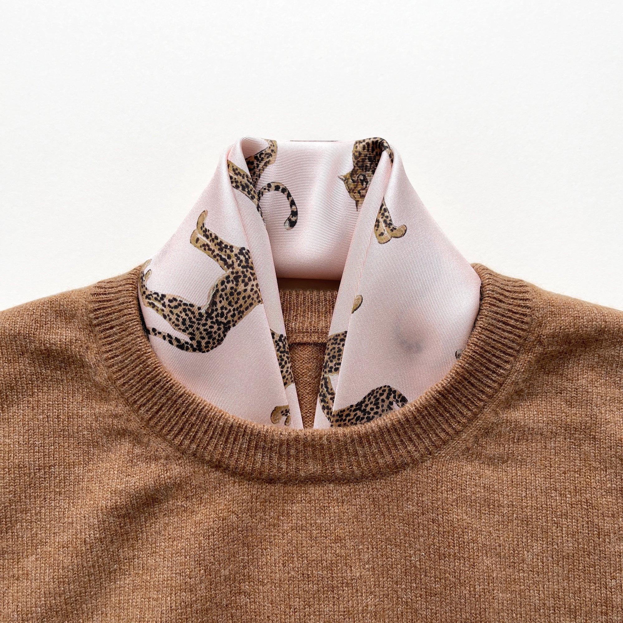 a pink base silk scarf featuring leopard print with red hand-rolled edges, tucked in a men's caramel sweater as a neck scarf