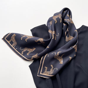 a black base silk scarf featuring leopard print with khaki brown hand-rolled edges, knotted as a neck scarf, paired with a women's black dress