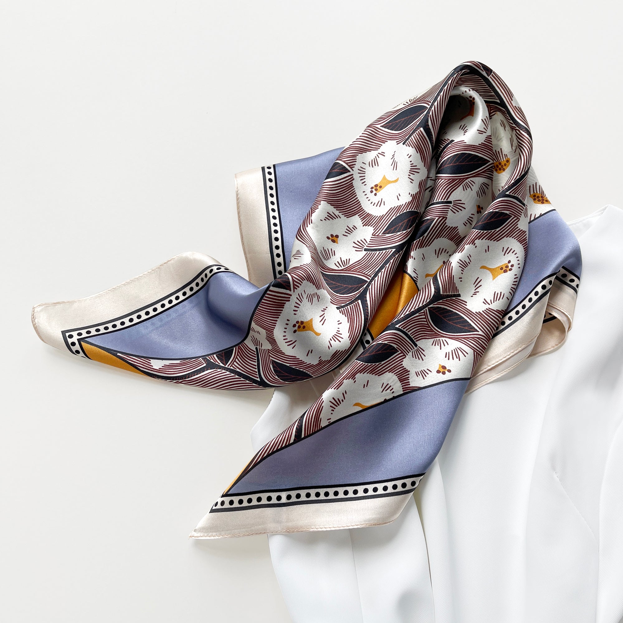 a women's silk scarf featuring white rock roses print with cornflower blue and orange edges, paired with a white dress