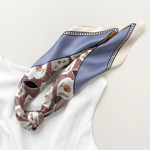 a women's silk scarf bandana featuring white rock roses print with cornflower blue and orange edges, knotted as a ponytail scarf, paired with a white dress