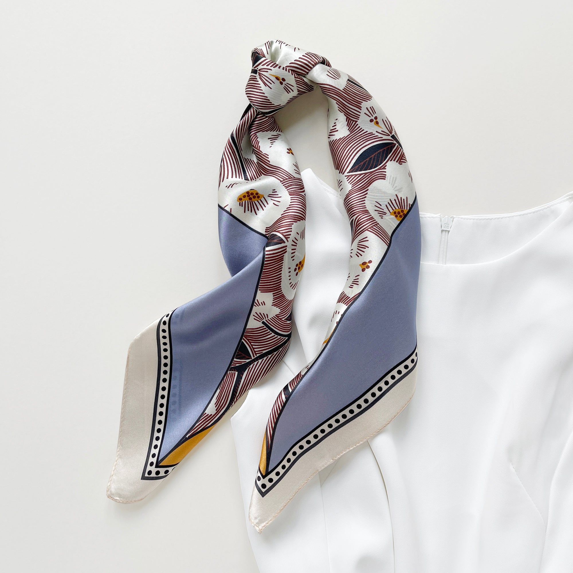 a women's silk scarf bandana featuring white rock roses print with cornflower blue and orange edges, knotted as a ponytail scarf, paired with a white dress