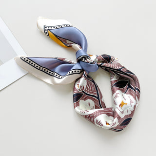 a women's silk scarf bandana featuring white rock roses print with cornflower blue and orange edges, knotted as a head scarf, paired with a white dress