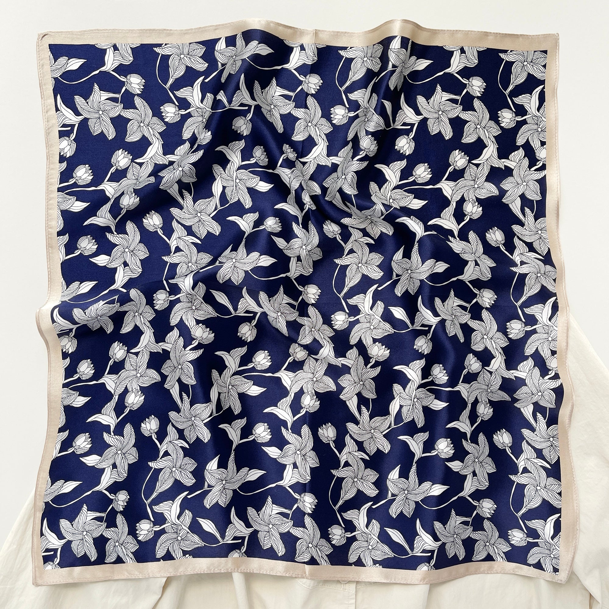 a deep blue silk bandana scarf featuring floral print with light beige edges