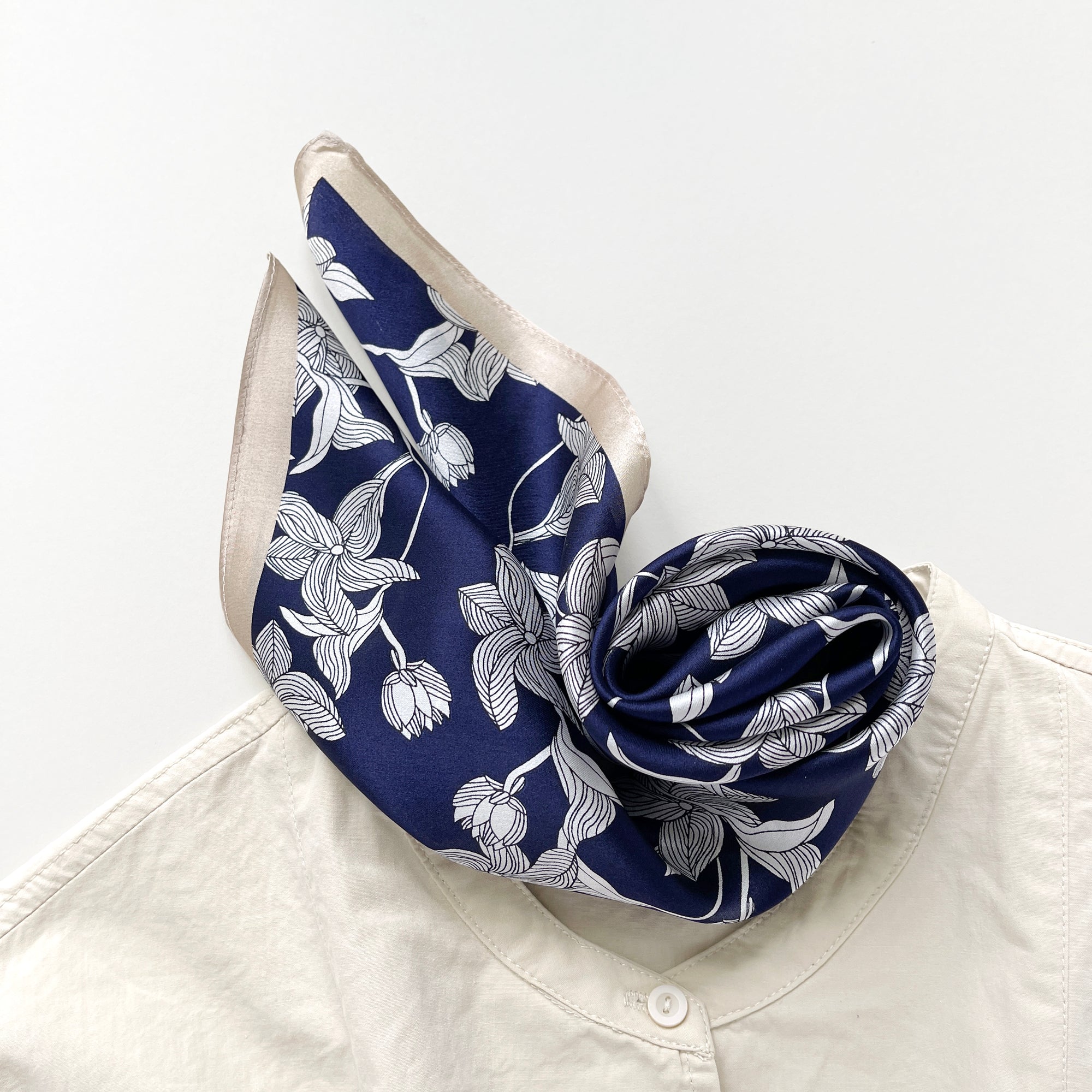 a deep blue silk bandana scarf featuring floral print with light beige edges, paired with a light beige turtleneck shirt