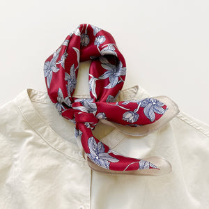 a burgundy red silk bandana scarf featuring floral print with light beige edge, tied as a neck scarf, paired with a light beige turtleneck shirt