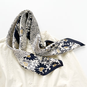 a women's black floral print silk scarf on light beige base, paired with a light beige turtleneck shirt