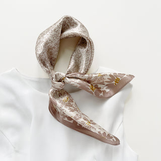 a women's pink beige floral print silk scarf on white base, knotted as a neck scarf, paired with a white dress