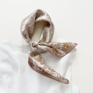 a women's pink beige floral print silk scarf on white base, knotted as a neck scarf, paired with a white dress