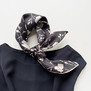 a black and white rose print silk bandana scarf with pink beige hand-rolled edges, tied as a neck scarf/neckerchief, paired with a black dress