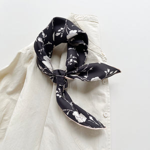 a black and white rose print silk bandana scarf with pink beige hand-rolled edges, tied as a neck scarf/neckerchief, paired with a women's light beige turtleneck shirt