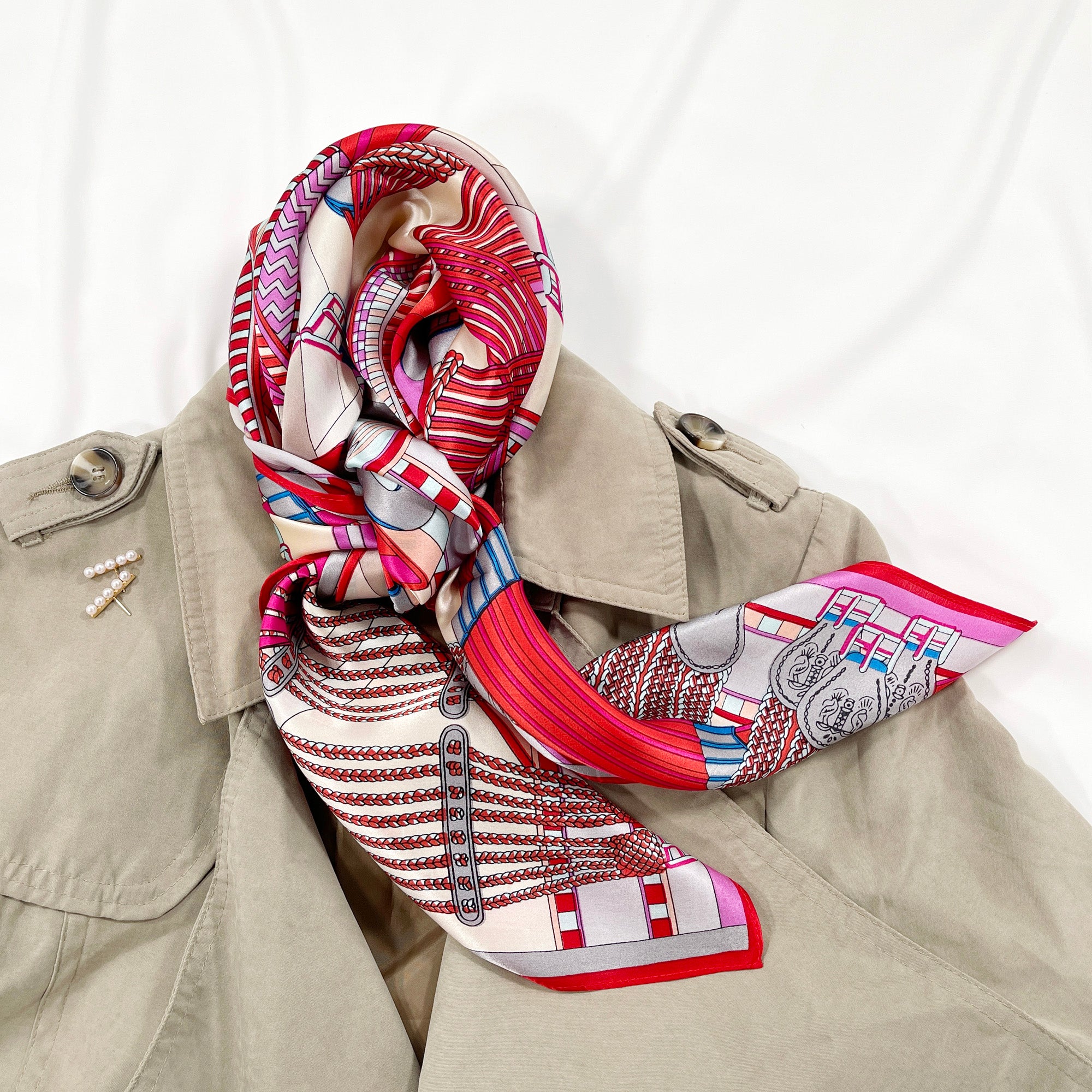 a vibrant silk scarf in magenta, red, ash grey and light beige palette knotted as a neck scarf, paired with beige coat