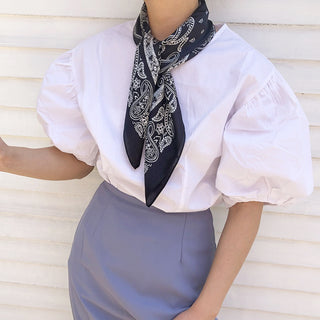 a women wearing a navy blue square silk scarf featuring white paisley print 