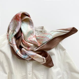 68x68 cm square silk scarf featuring a soft, light beige background with an intricate floral pattern of hibiscus flowers and butterflies. The flowers are outlined in shades of cream, red, and green, complemented by delicate leaves. The scarf has a wide, brown border framing the design.