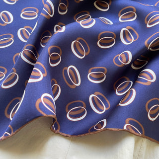 Indigo purple unisex silk bandana scarf with a circular pattern, made from 100% silk twill, featuring hand-rolled edges. The scarf measures 53x53cm and is designed for both men and women.