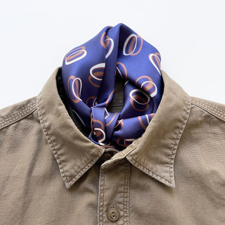 Indigo purple unisex silk bandana scarf with a circular pattern, made from 100% silk twill, featuring hand-rolled edges. The scarf measures 53x53cm and is designed for both men and women.