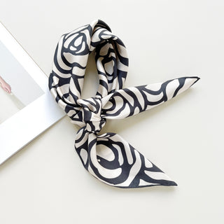 a white base women's silk scarf with deep charcoal grey abstract rose print and hand-rolled edges, knotted as a neck scarf