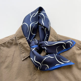 65x65 cm navy blue silk scarf with a geometric pattern and hand-rolled edges, designed for both men and women. The scarf features a smooth silk texture and is accented with elegant white wave-like lines, perfect for versatile styling.