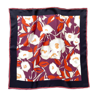 A 100% silk twill bandana with hand-rolled edges, featuring a floral design with white flowers and orange leaves on a burgundy  purple background framed by a black border