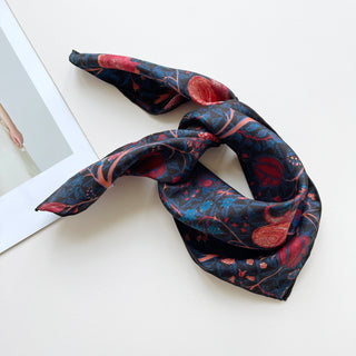 Deep blue floral silk bandana scarf with hand-rolled edges styled in a loose knot. The luxurious 100% silk fabric features a detailed red and pink floral pattern, perfect for adding an elegant touch to any outfit.