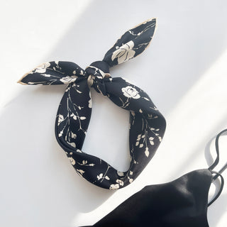 a black and white rose print silk bandana scarf with pink beige hand-rolled edges, knotted as a headband