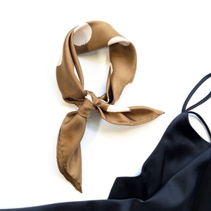 a brown beige polka dot silk scarf with hand-rolled hems knotted as a neckerchief next to a black dress