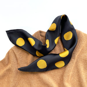a black silk twill scarf with golden polka dot laying on a caramel cashmere sweater