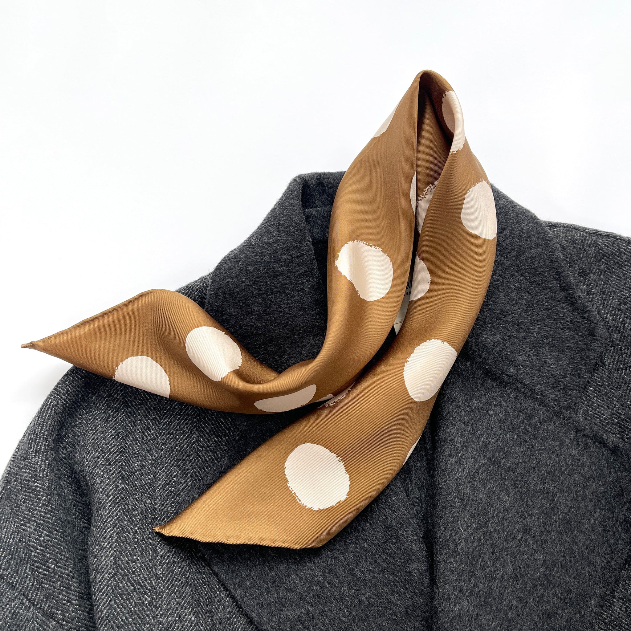 a brown beige polka dot silk twill scarf with hand-rolled hems laying on a dark grey wool coat