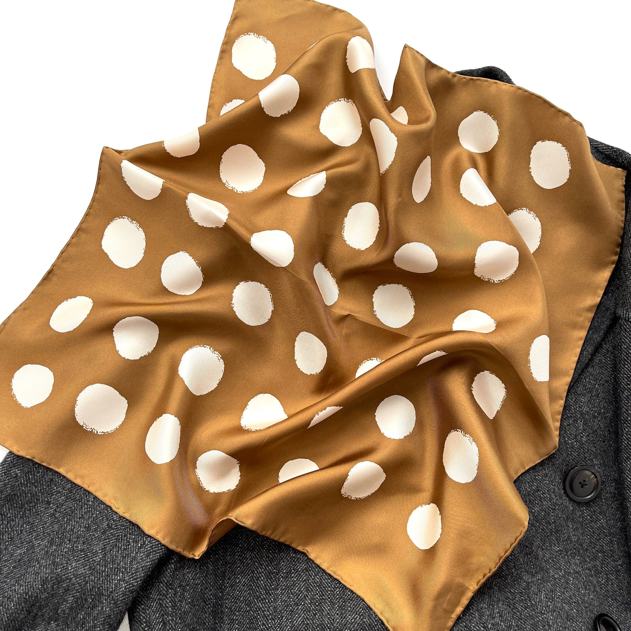 a brown beige polka dot square silk twill scarf with hand-rolled hems laying on a dark grey wool coat