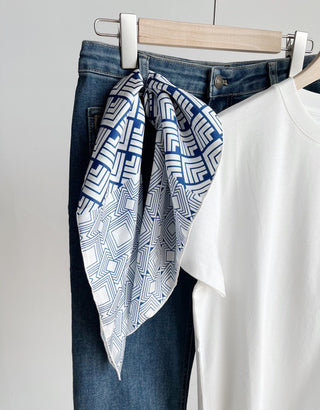 a white base bandana silk scarf featuring blue geometric pattern with hand-rolled edges, paired with a white t-shirt and blue jeans