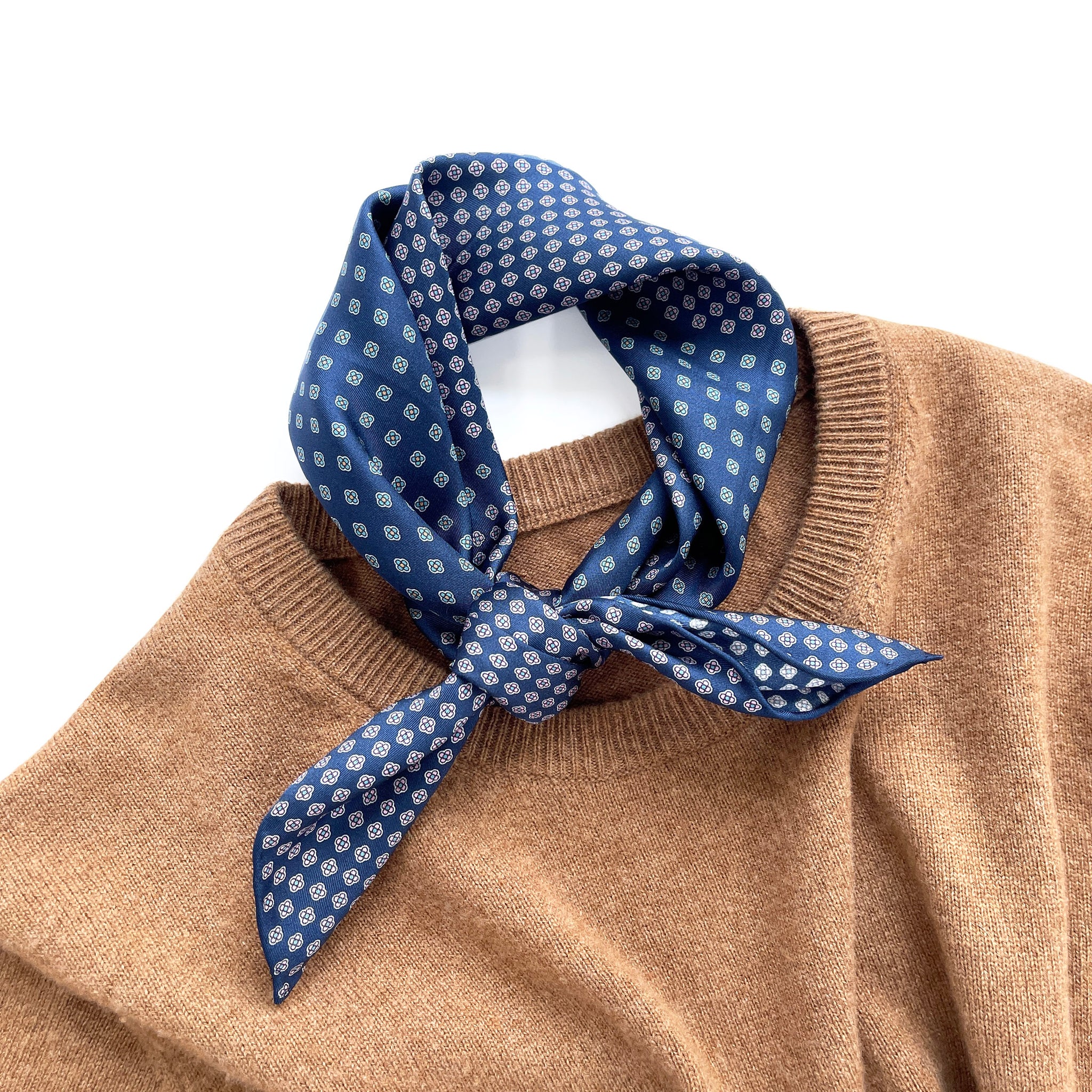 a navy blue men's silk scarf with hand-rolled hems featuring four leaf clover print knotted as a neckerchief, laying on a caramel cashmere sweater