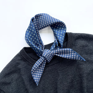 a navy blue men's silk scarf with hand-rolled hems featuring four leaf clover print knotted as a neckerchief, laying on a dark grey mens sweater