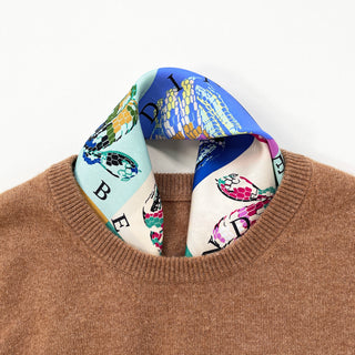 A vibrant square silk scarf with swirling snakes print tucked into a caramel cashmere sweater as neck scarf.