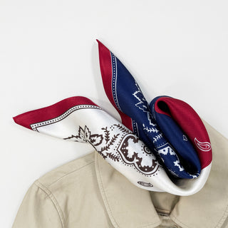 a bohemian paisley silk scarf in blue, red and white palette laying on a beige coat