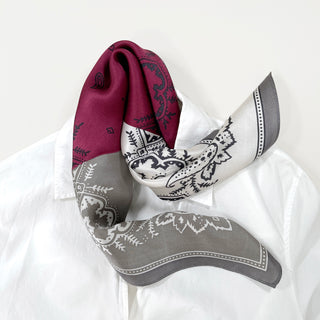 a bohemian paisley silk scarf in plum red, grey and white palette laying on a white shirt 