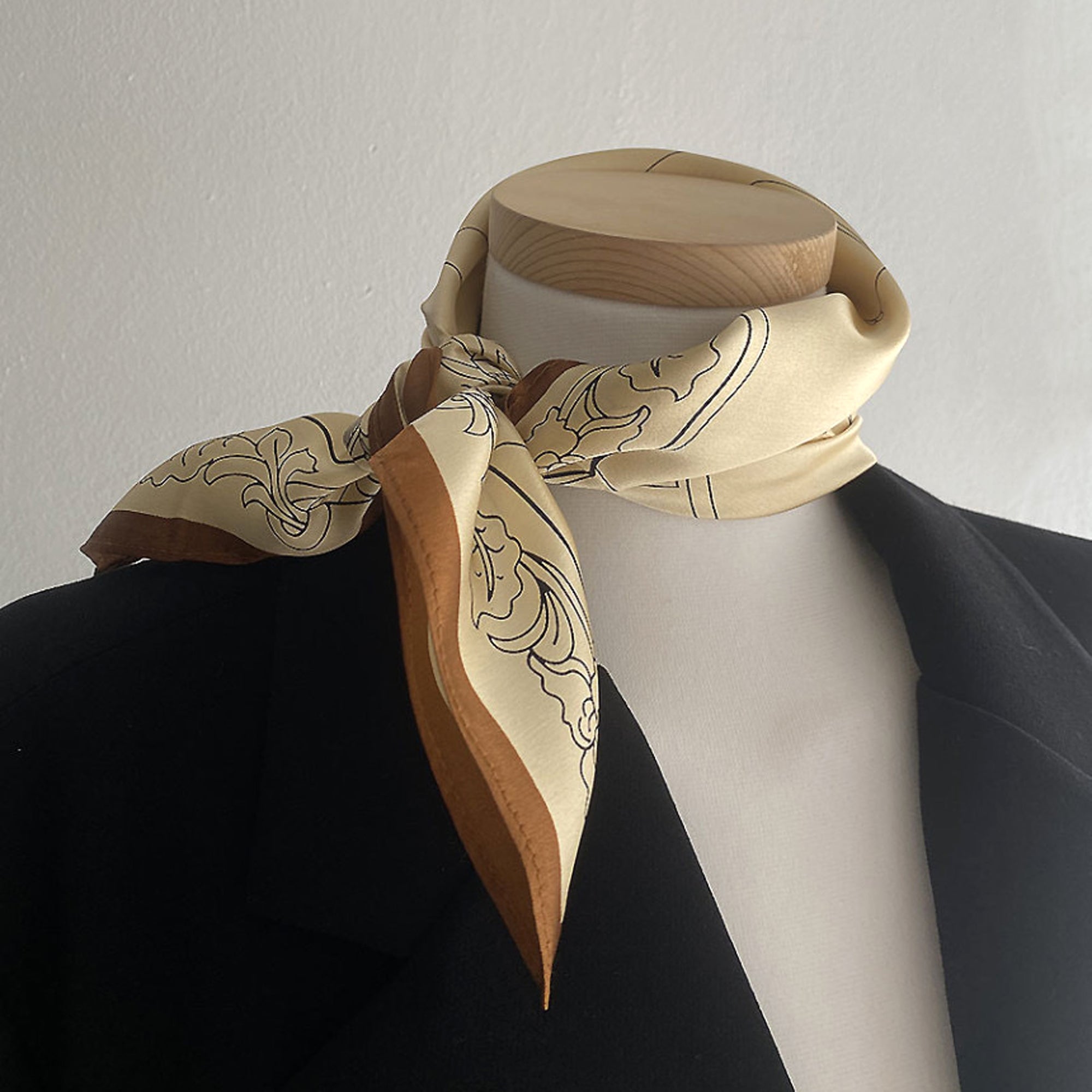 a timeless pale apricot silk bandana scarf featuring black print with brown edge tied as a classic neck scarf, paired with a black blouse