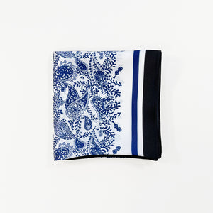 a white based silk scarf with rich blue paisley pattern print folded as a small square