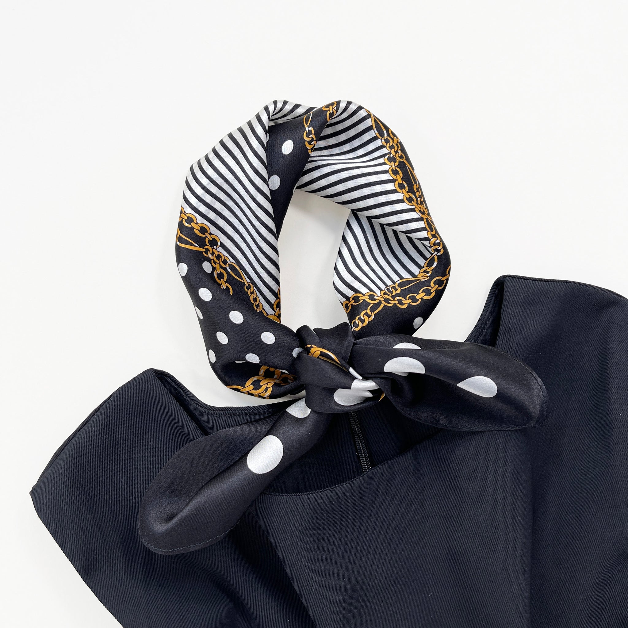 a small square silk scarf for women featuring polka dot and stripe print in black and white palette knotted as a neckerchief paired with a sleeveless black dress