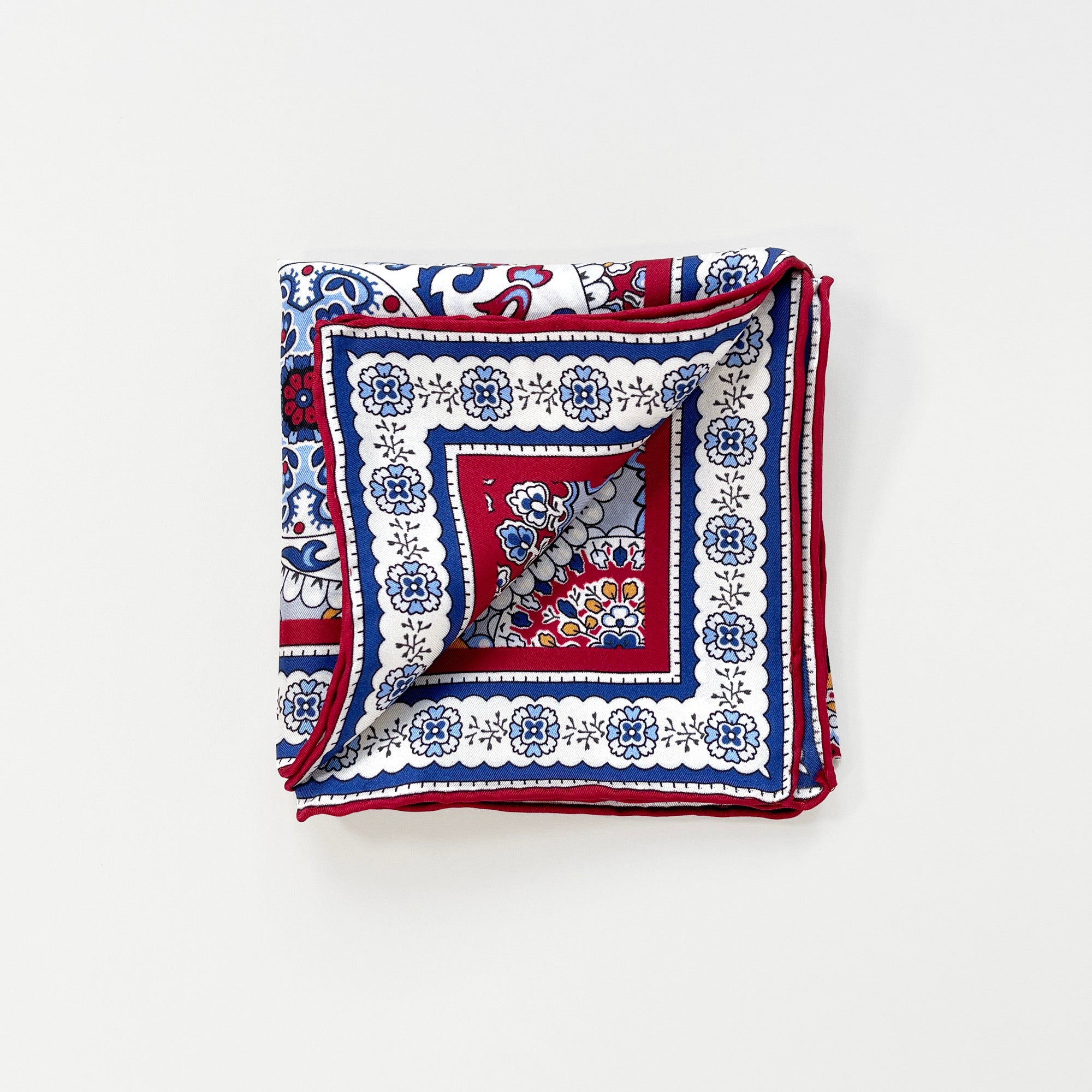 a folded red, blue and yellow silk scarf square for men featuring boho-style print and red hand-rolled hems