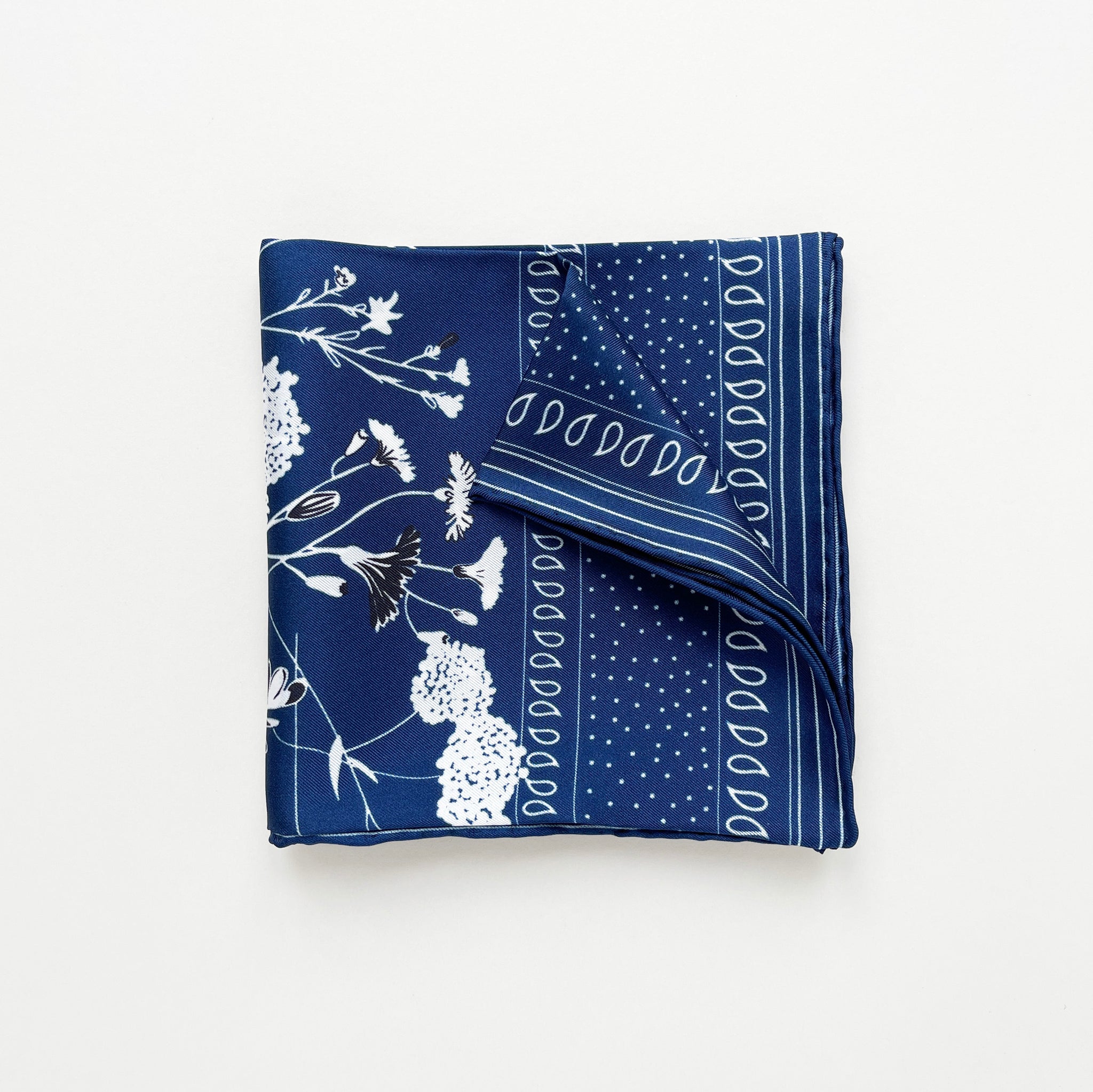 a folded rich blue silk scarf featuring botanic leafy and flower print and hand-rolled hems