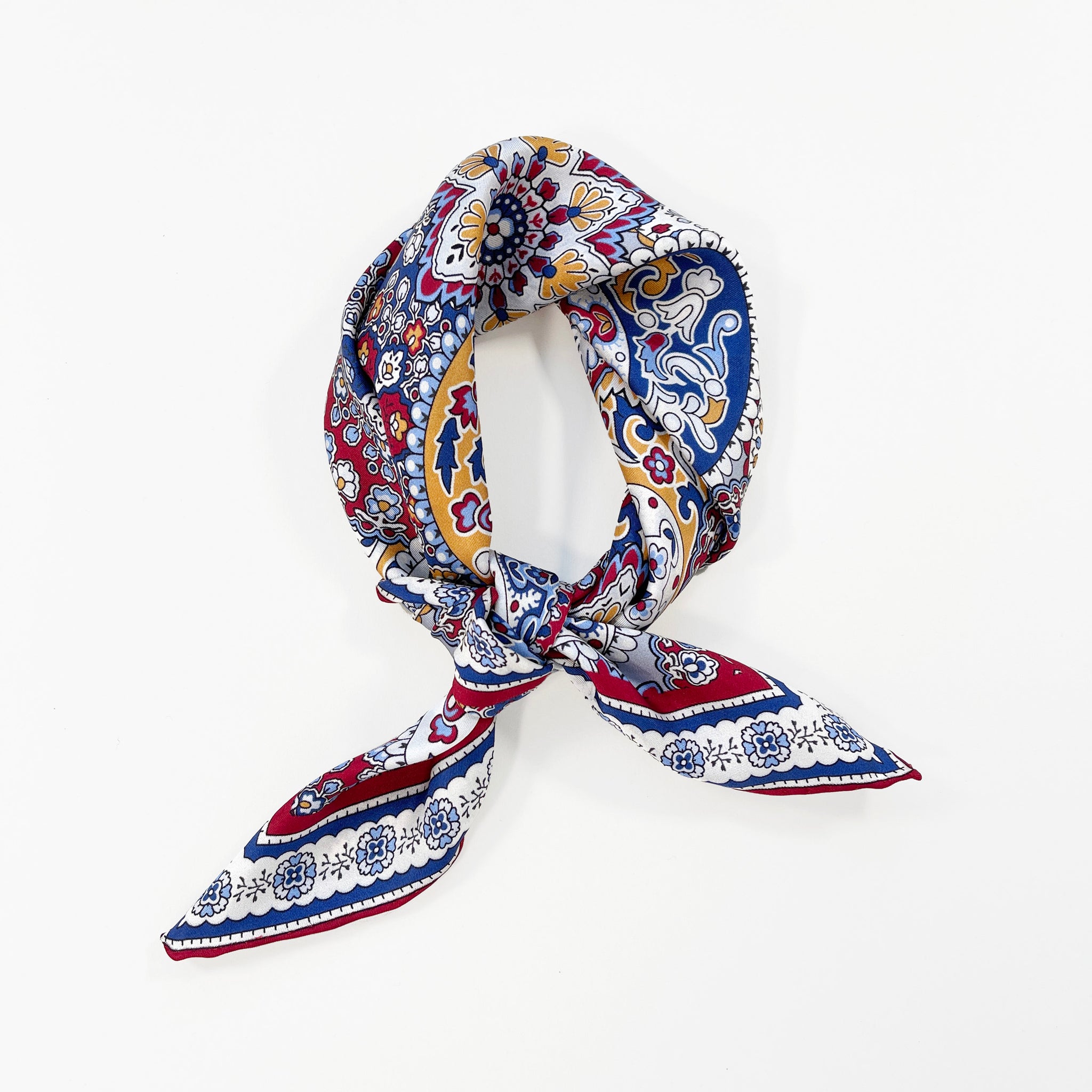 a red, blue and yellow silk scarf square for men featuring boho-style print and red hand-rolled hems knotted as a neckerchief